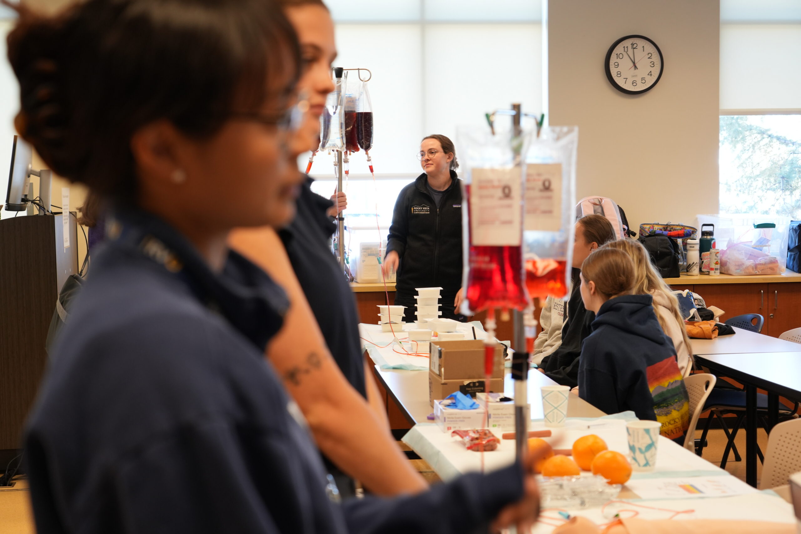 Two RVU students face a classroom with an IV drip prop from Simulation in Medicine in the background